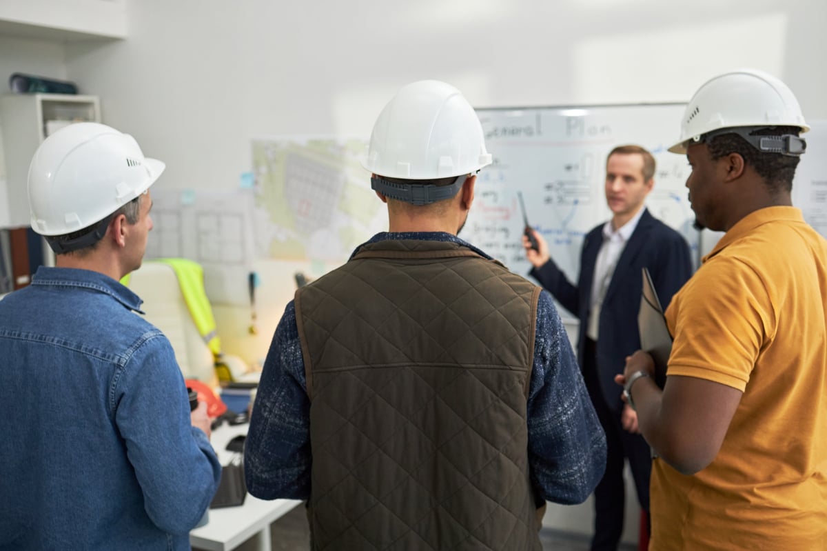 Construction foremen reviewing a safety and risk management plan with a supervisor in an office